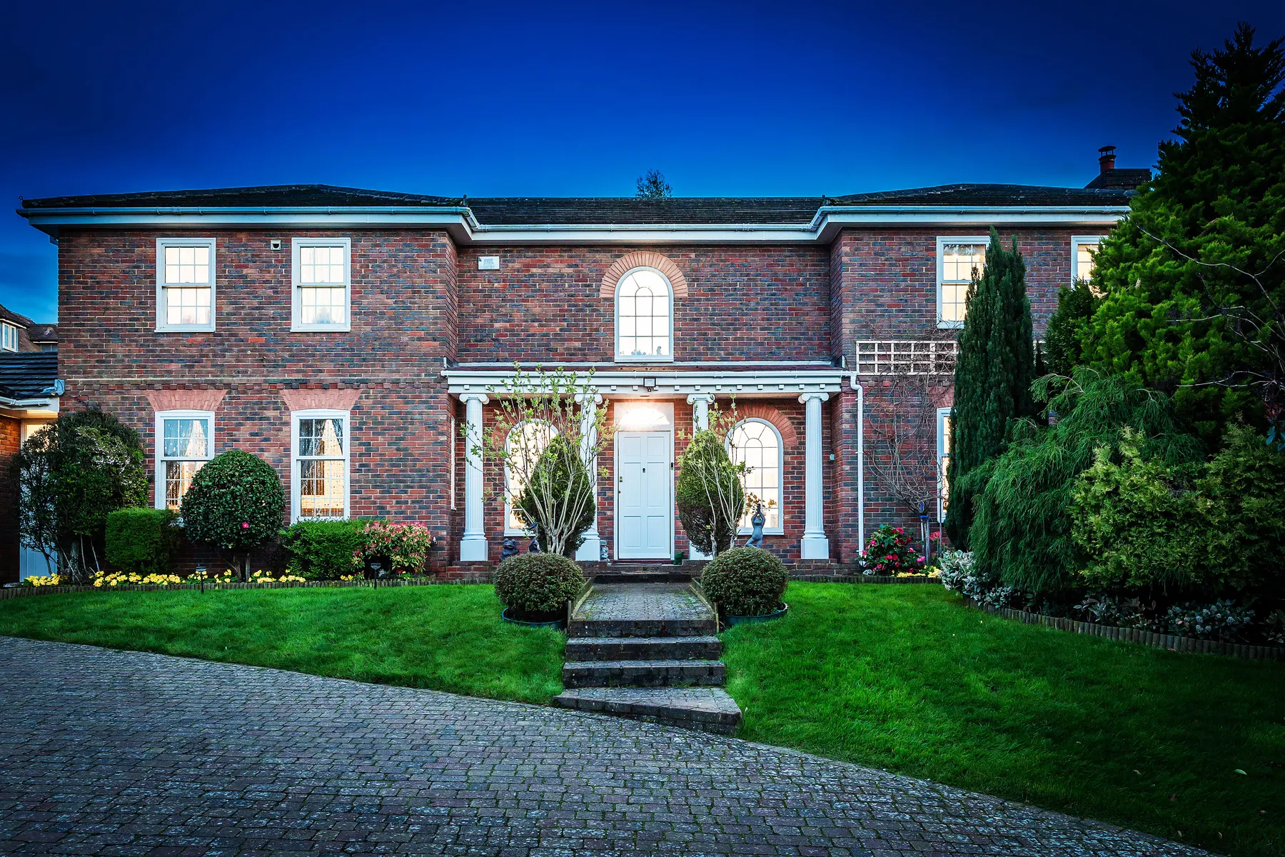 A formal red-brick family home in Tunbridge Wells at dusk, lit from within.